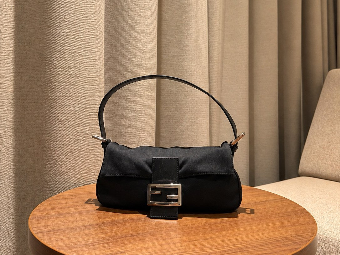 Sac Fendi Baguette noir en satin, posé sur une table ronde en bois devant un rideau sable
